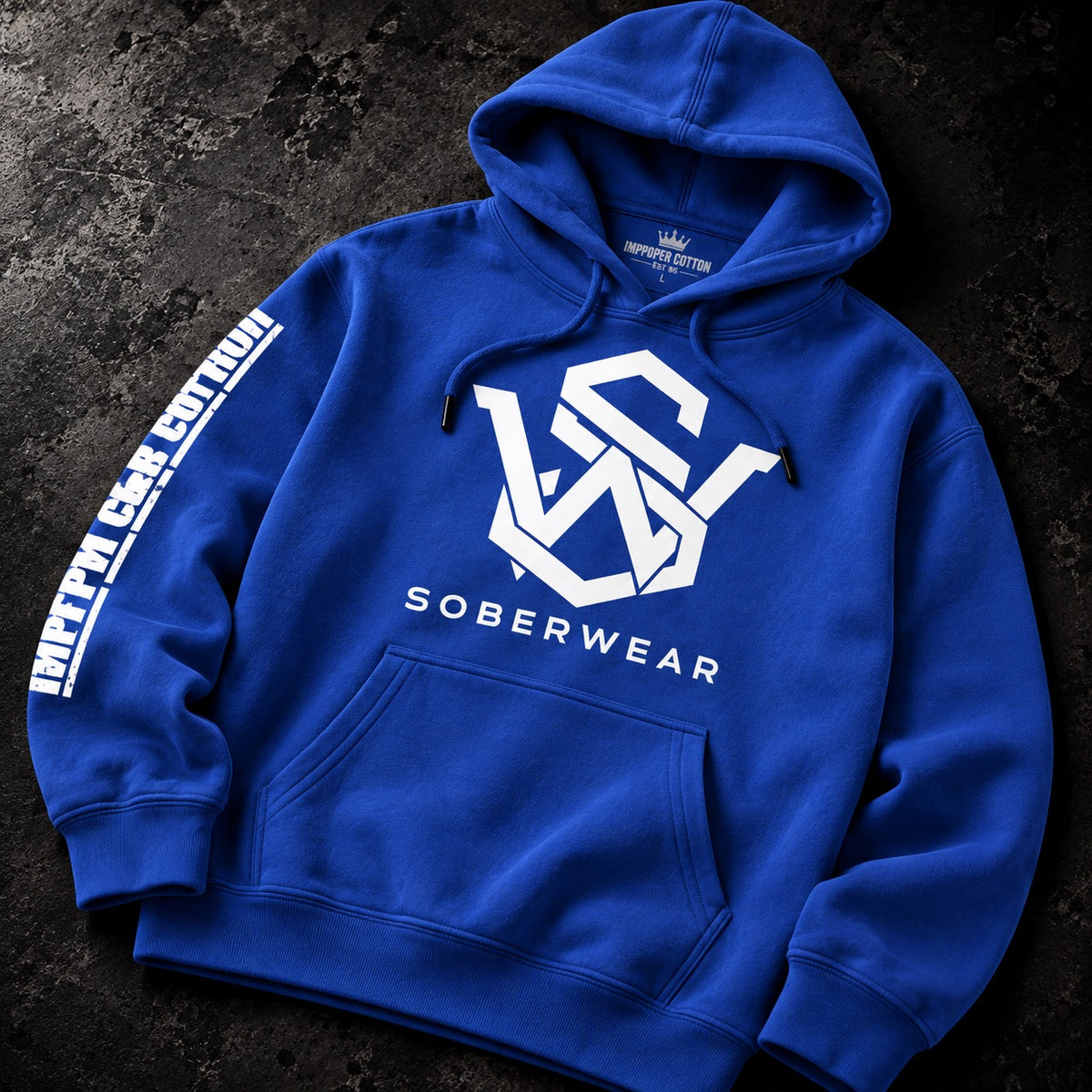 A royal blue pullover hoodie laid flat on a dark textured surface. The hoodie features a large white geometric 'VS' logo on the chest with 'SOBERWEAR' printed underneath, a white vertical sleeve print reading 'INFLATED CASH CLOTHING' on the right sleeve, and a small white crown logo on the inner neck label.