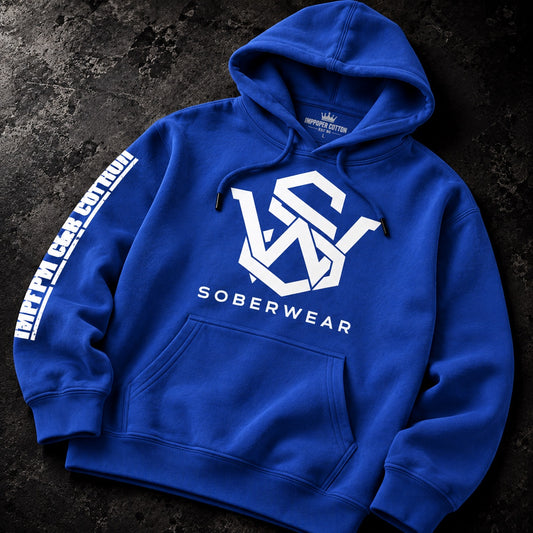 A royal blue pullover hoodie laid flat on a dark textured surface. The hoodie features a large white geometric 'VS' logo on the chest with 'SOBERWEAR' printed underneath, a white vertical sleeve print reading 'INFLATED CASH CLOTHING' on the right sleeve, and a small white crown logo on the inner neck label.