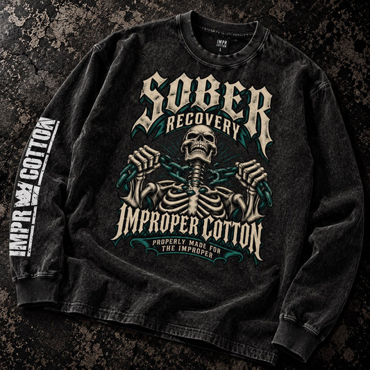 A black acid-wash long-sleeve t-shirt with a detailed gothic graphic of a skeleton and the text 'Sober Recovery Improper Cotton' on the front, with 'Improper Cotton' printed vertically on the sleeve, laid flat on a dark textured background.