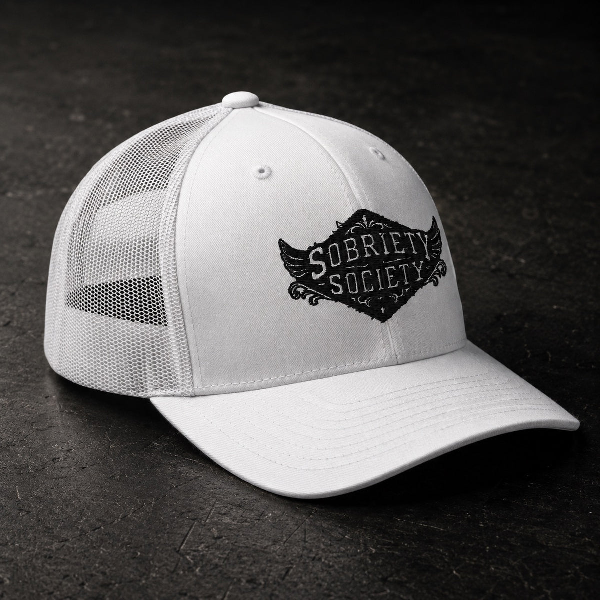 A white trucker-style cap with a black embroidered 'Sobriety Society' logo on the front panel, shown on a dark textured background.