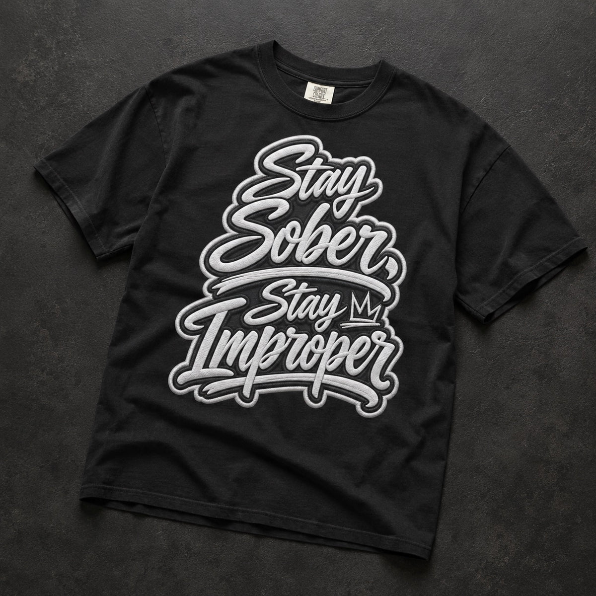 A black short-sleeve t-shirt with a large white and gray graphic text reading 'Stay Sober, Stay My Improper' laid flat on a dark textured background.