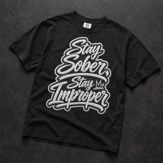 A black short-sleeve t-shirt with a large white and gray graphic text reading 'Stay Sober, Stay My Improper' laid flat on a dark textured background.