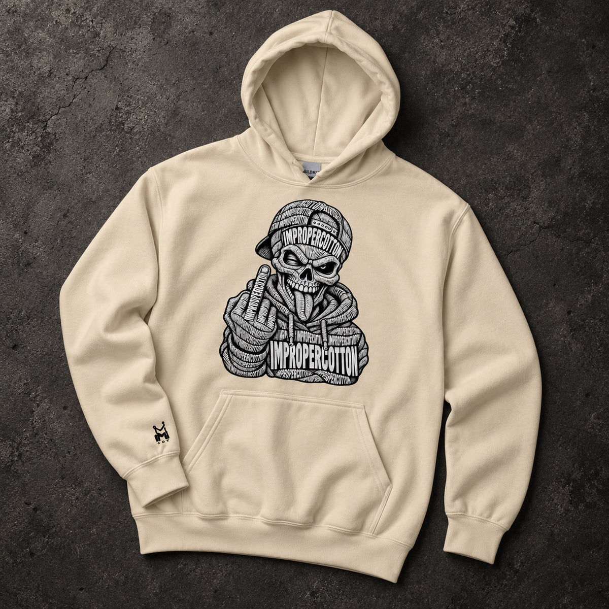 A cream-colored pullover hoodie with a detailed black graphic of a skull wearing a cap and hoodie, making a middle finger gesture, with the words 'IMPROPERCOTTON' and 'IMPROPERLY COTTON' on the graphic. The hoodie is laid flat on a dark textured background.