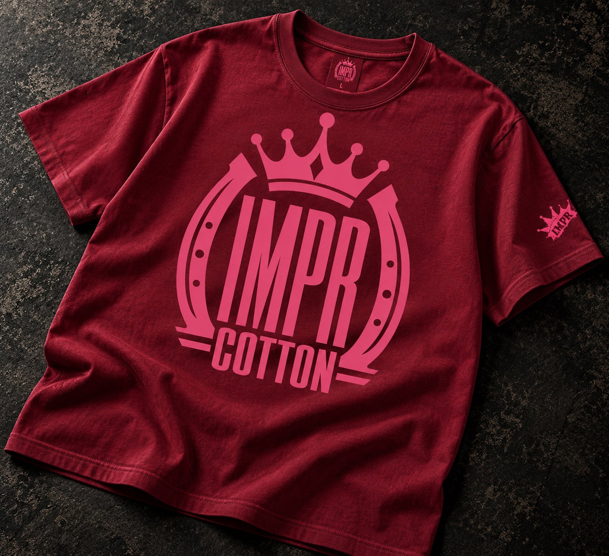Wine red iMPR cotton crown premium graphic tee shirt laying on a dark textured table 