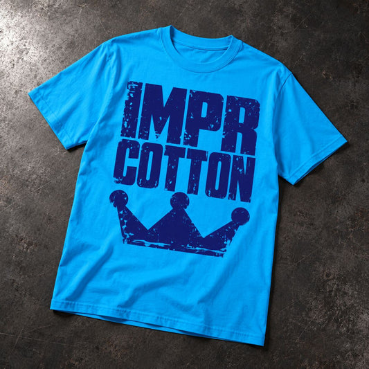 A bright blue short-sleeve t-shirt laid flat on a dark textured surface, featuring a distressed dark blue graphic that reads 'IMPR COTTON' above a crown silhouette.