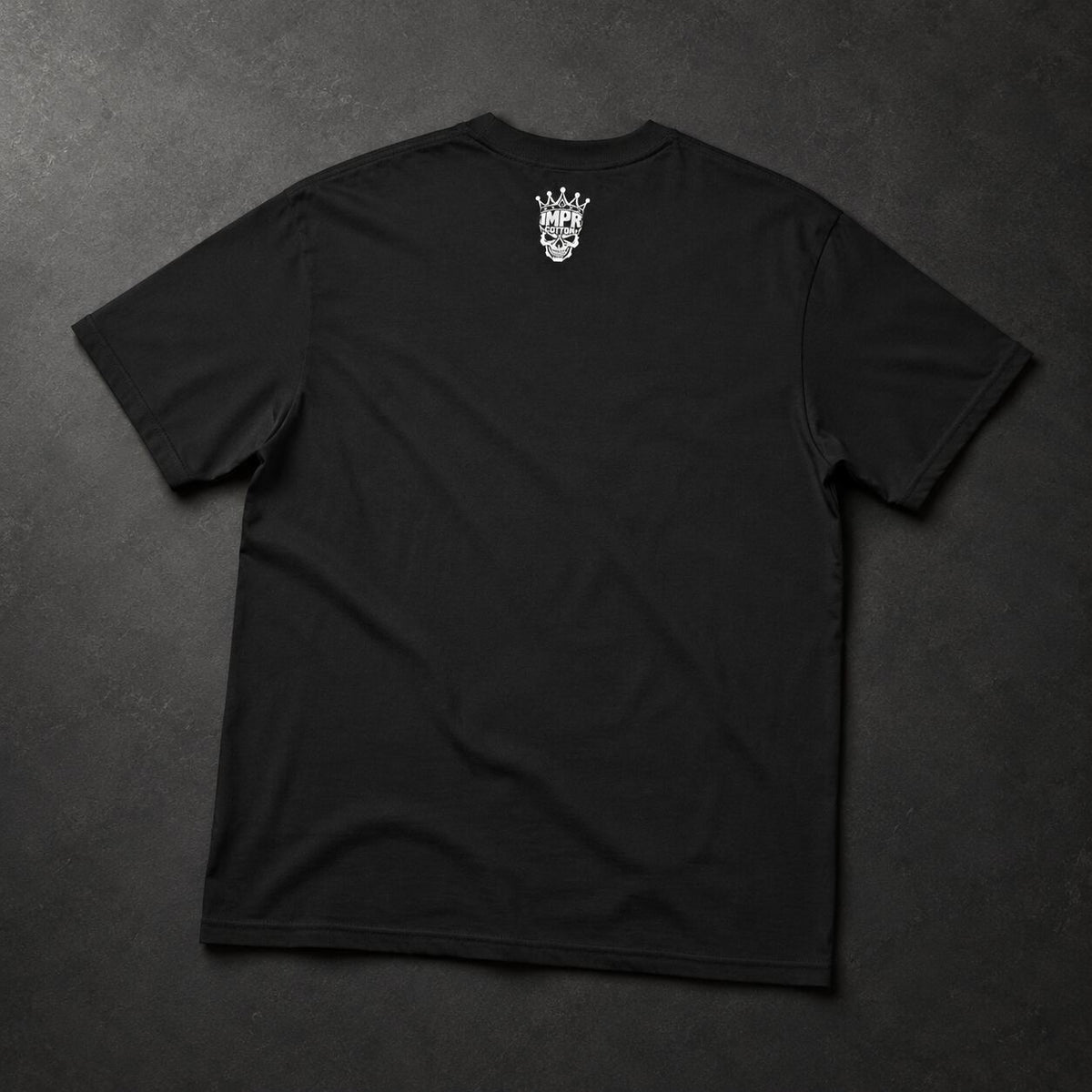 A black short-sleeve t-shirt laid flat on a dark textured background, featuring a small white graphic of a skull wearing a crown printed on the upper back.
