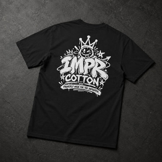A black short-sleeve t-shirt laid flat on a dark textured background, featuring a large white graphic print on the back with the words 'IMPR COTTON' and a crown illustration.