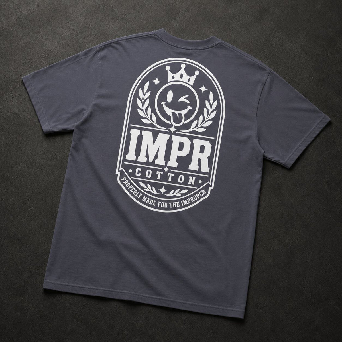 A dark gray crewneck t-shirt shown from the back, featuring a large white graphic print with a crown, laurel wreath, and the text 'IMPR COTTON' and 'PROPERLY MADE FOR THE IMPROPER'.