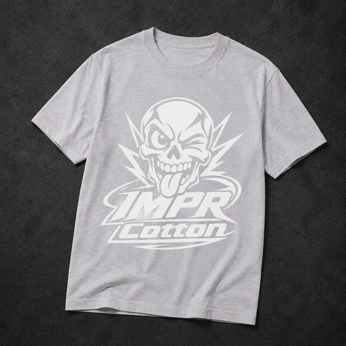 A light gray heather crewneck t-shirt featuring a large white graphic of a skull with its tongue sticking out, above the text 'IMPR Cotton', laid flat on a dark textured background.