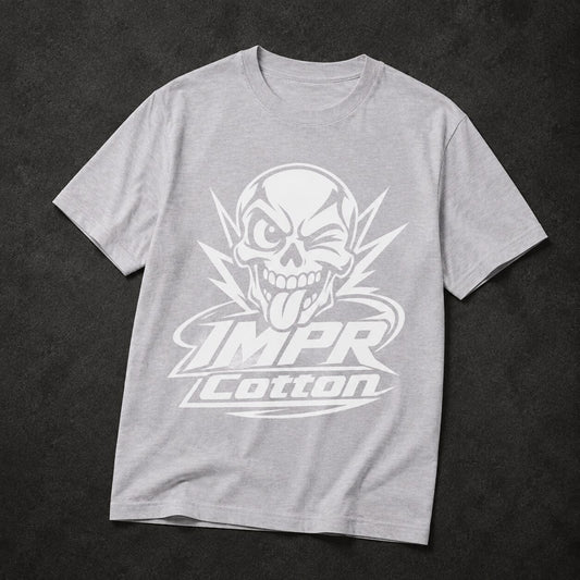 A light gray heather crewneck t-shirt featuring a large white graphic of a skull with its tongue sticking out, above the text 'IMPR Cotton', laid flat on a dark textured background.