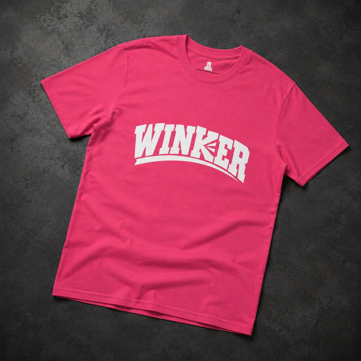 A bright pink short-sleeve t-shirt with 'WINKER' printed in bold white arched letters across the chest, laid flat on a dark textured background.