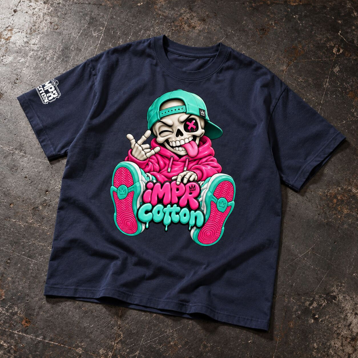 A navy blue graphic t-shirt laid flat on a textured, dark gray concrete-like surface. The shirt features a large cartoon graphic of a skeleton wearing a pink hoodie and a green cap, with the text 'IMP Cotton' in pink and green.