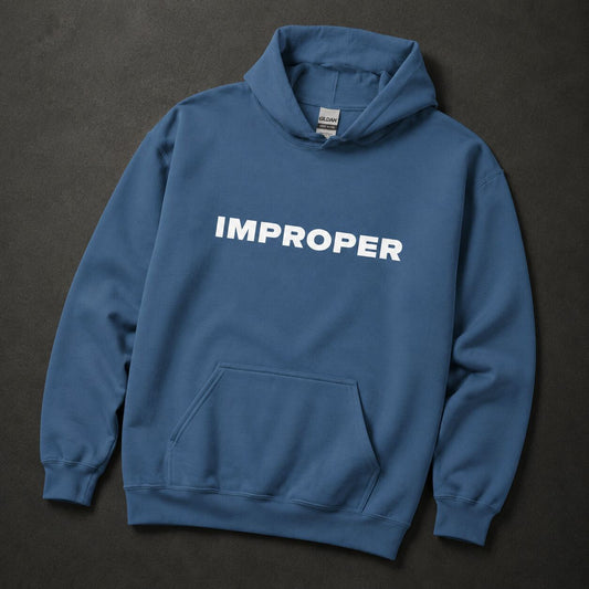 A slate blue pullover hoodie with the word 'IMPROPER' printed in bold white capital letters across the chest, laid flat on a dark textured background.