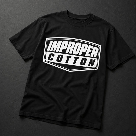 A black short-sleeve t-shirt with a white graphic print on the front that reads 'IMPROPER COTTON' inside a shield-like border, laid flat on a dark textured background.