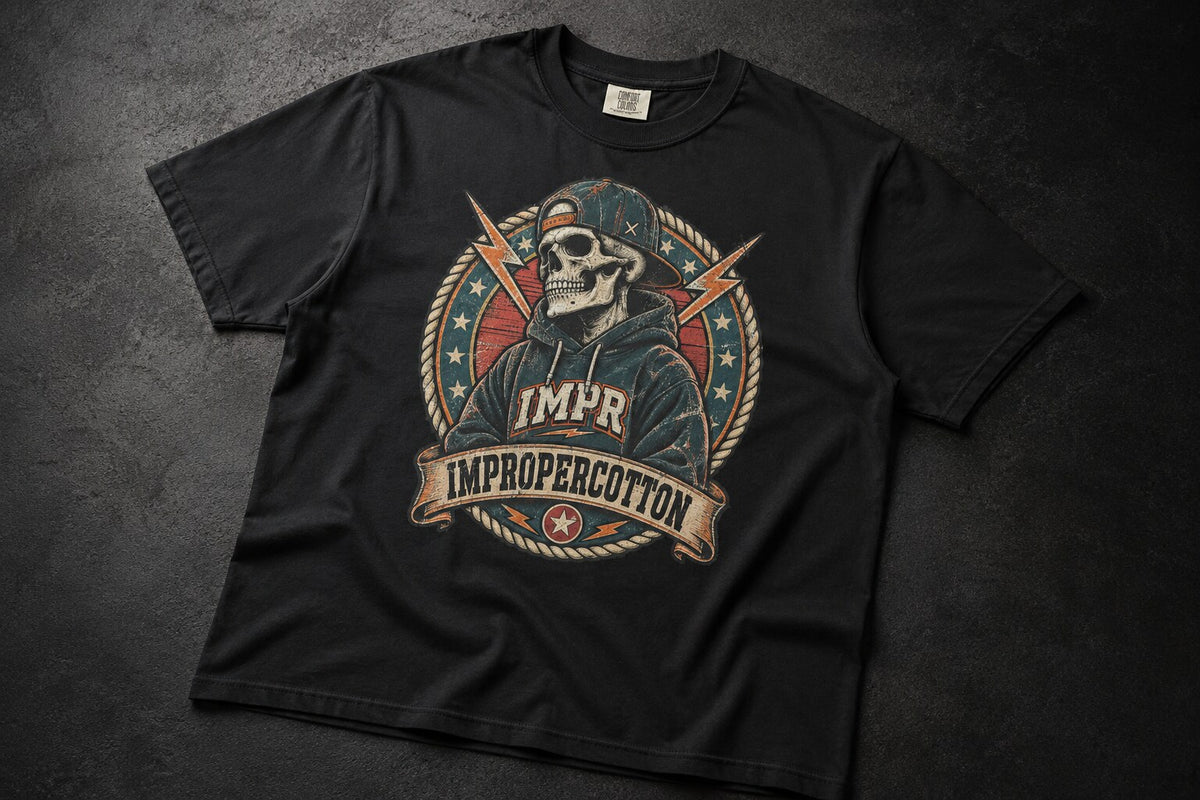 A black short-sleeve graphic t-shirt laid flat on a dark textured background. The front features a circular graphic of a skull wearing a cap, surrounded by ropes, stars, lightning bolts, and a banner that reads 'IMPR IMPROPERCOTTON'.