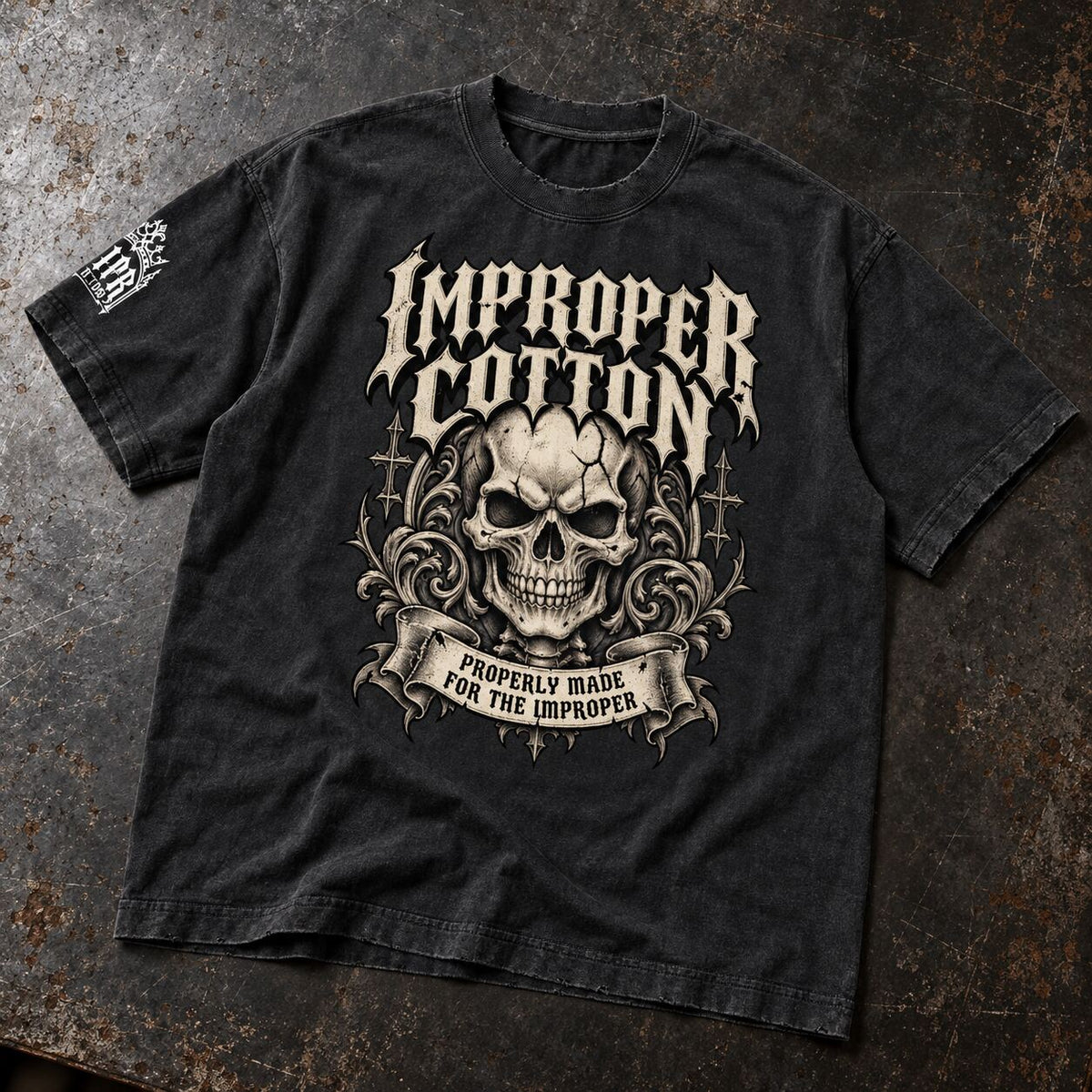 A black washed graphic t-shirt laid flat on a textured, dark rustic surface. The shirt features a large front graphic with a skull, ornate flourishes, and the text 'IMPROPER COTTON' and 'PROPERLY MADE FOR THE IMPROPER'.