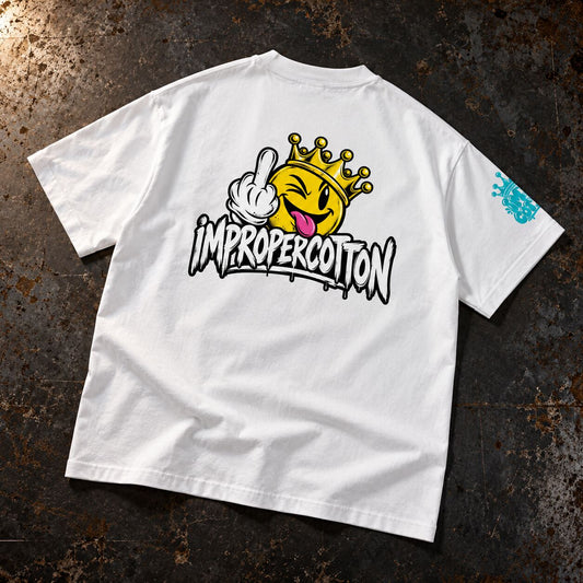 A white short-sleeve t-shirt laid flat on a dark, textured metal surface. The back of the shirt features a large graphic of a yellow crown emoji with a hand gesture and the text 'IMPROPERCOTTON' in a stylized font.