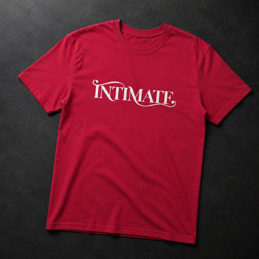 A red short-sleeve crewneck t-shirt with the word 'INTIMATE' printed in white cursive across the chest, laid flat on a dark textured background.