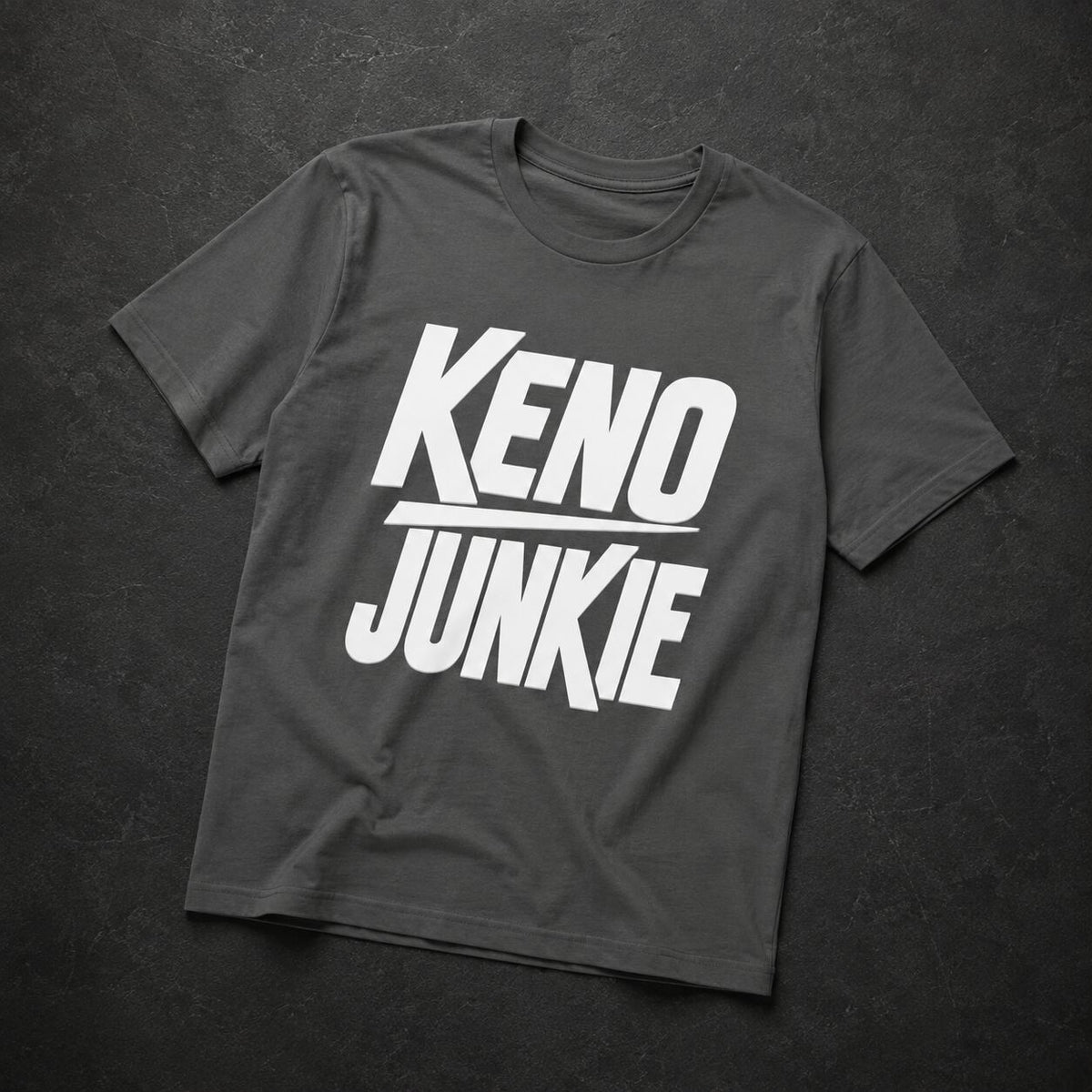 A dark gray crewneck t-shirt with a bold white graphic reading 'KENO JUNKIE' across the chest, laid flat on a dark textured background.