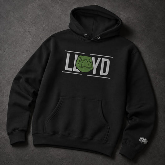 A black pullover hoodie laid flat on a dark textured background, featuring a front graphic that reads 'LLOYD' with a green frog head inside the letter O, and a small white sleeve patch.