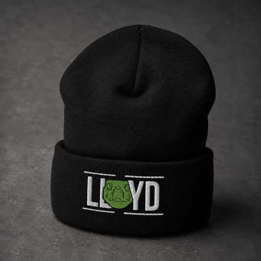 A black knit beanie hat with a folded cuff, featuring white embroidered text reading 'LLOYD' and a green frog emblem, photographed on a dark textured surface.