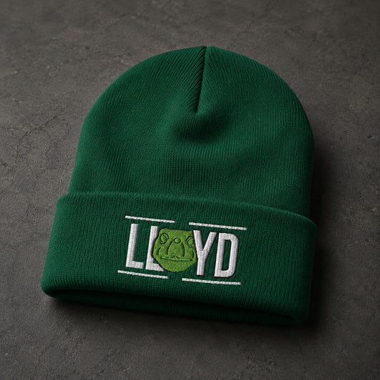 A dark green knit beanie hat with a folded cuff, featuring an embroidered logo that reads 'LLOYD' with a green frog emblem, placed on a dark textured surface.