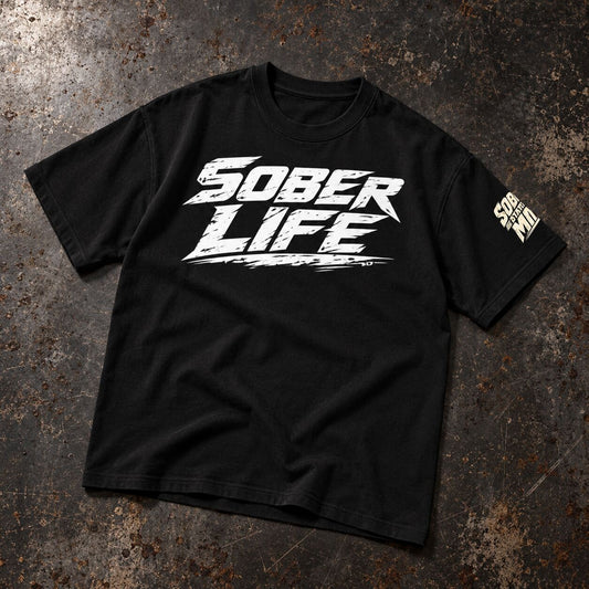 A black short-sleeve t-shirt with a distressed white 'SOBER LIFE' graphic on the chest and a small vertical white graphic on the right sleeve, laid flat on a textured dark gray and brown surface.