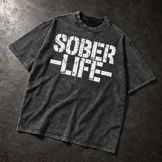 A dark gray acid-wash t-shirt with a distressed white graphic reading 'SOBER LIFE' laid flat on a dark textured background.