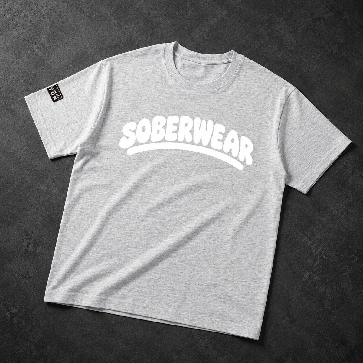 A light heather gray crewneck t-shirt with 'SOBERWEAR' printed in white across the chest, laid flat on a dark textured background.