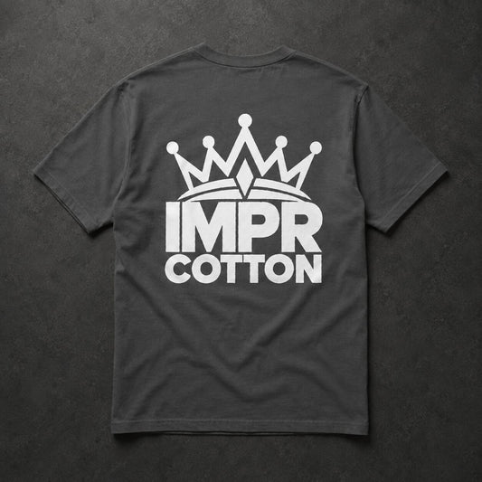 A dark gray t-shirt laid flat on a dark textured background, featuring a white graphic of a crown above the text 'IMPR COTTON' on the back.