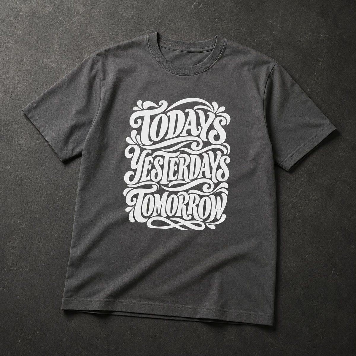 A dark charcoal gray t-shirt with a white graphic print reading 'TODAY'S YESTERDAYS TOMORROW' in an ornate, hand-lettered style, laid flat on a dark textured background.